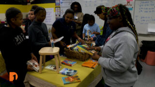Students at Voyageur Academy in Southwest Detroit gather around a table looking at books during a book fair hosted by Birdie's Bookmobile.